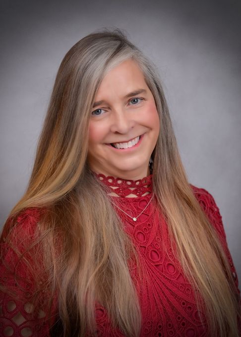 A woman with long hair is wearing a red sweater and smiling for the camera.