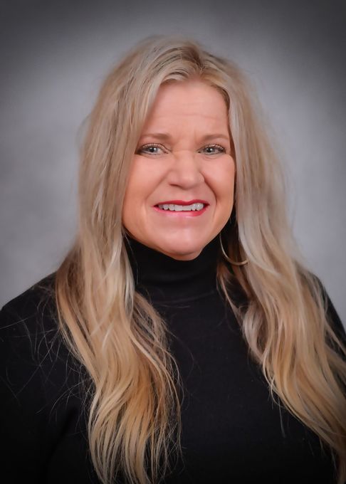 A woman with long blonde hair is wearing a black turtleneck and smiling.