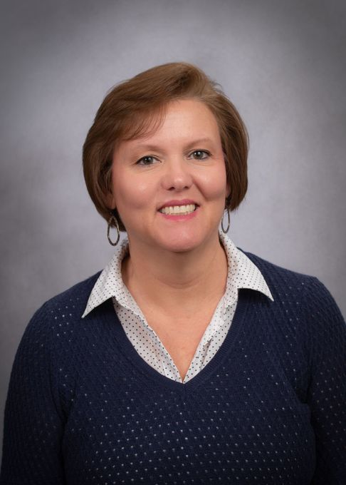 A woman in a blue sweater and white shirt is smiling for the camera.