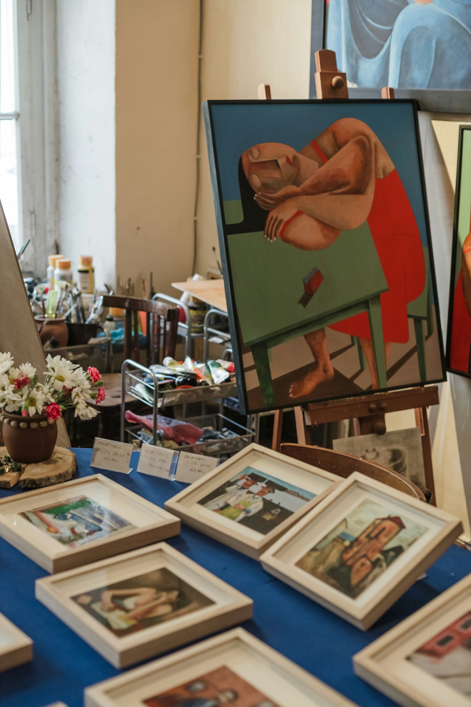 A painting of a woman sitting at a table is on an easel