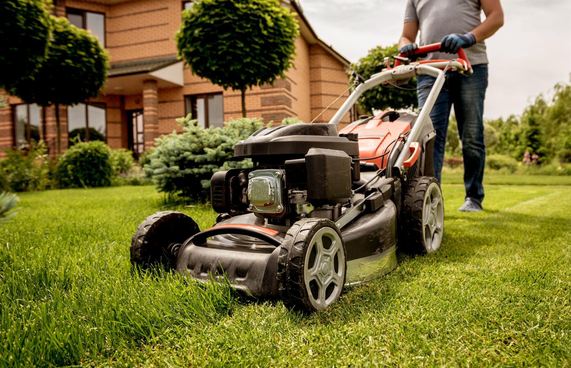 Person mowing a green lawn with a push mower beside a house