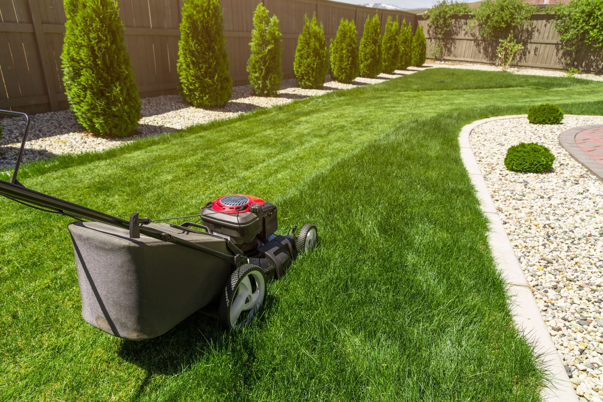 Lawn mower on a neatly trimmed green lawn beside a curving white gravel path and landscaped shrubs