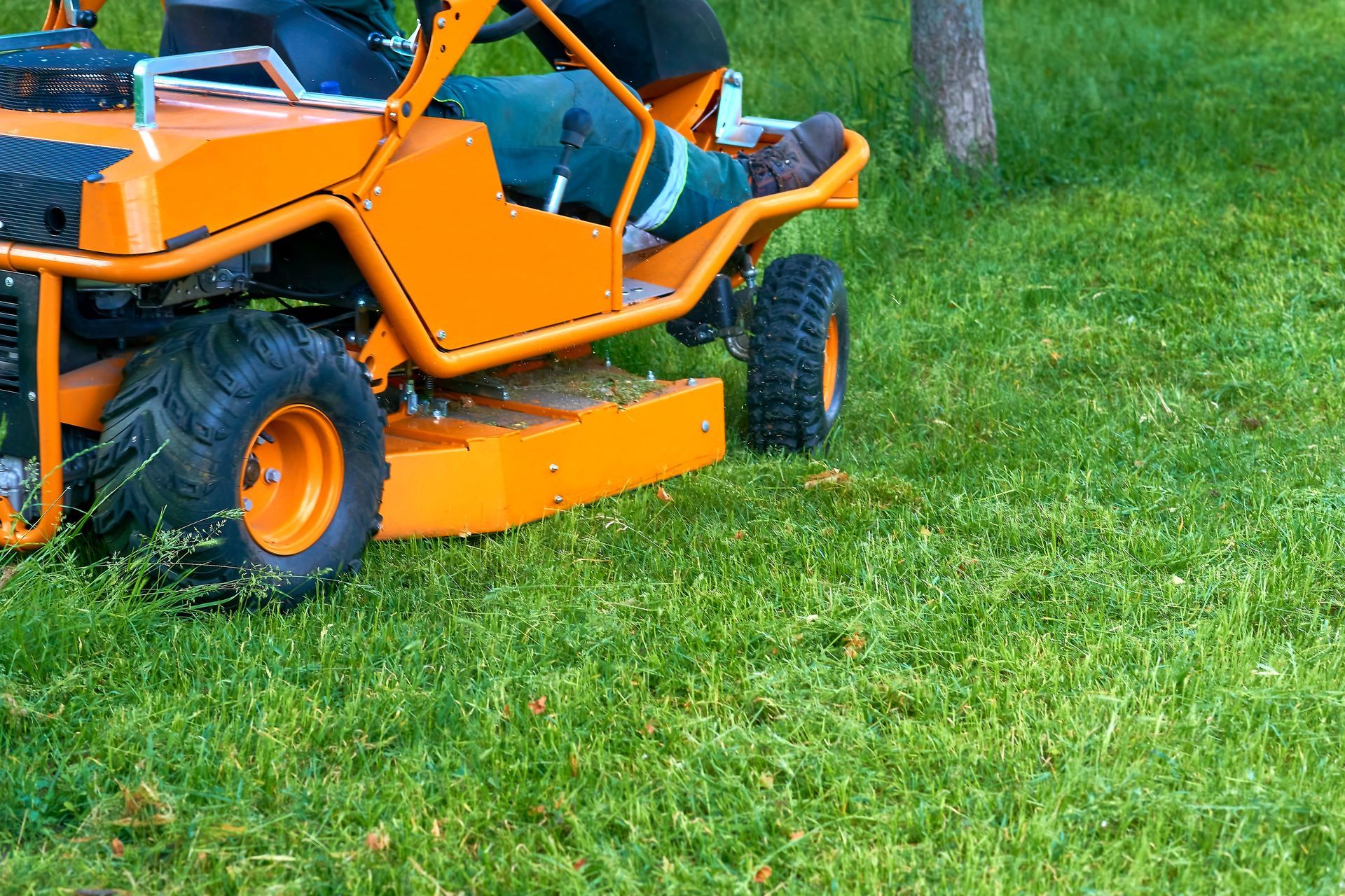 Orange lawn mower on green grass, cutting a lawn
