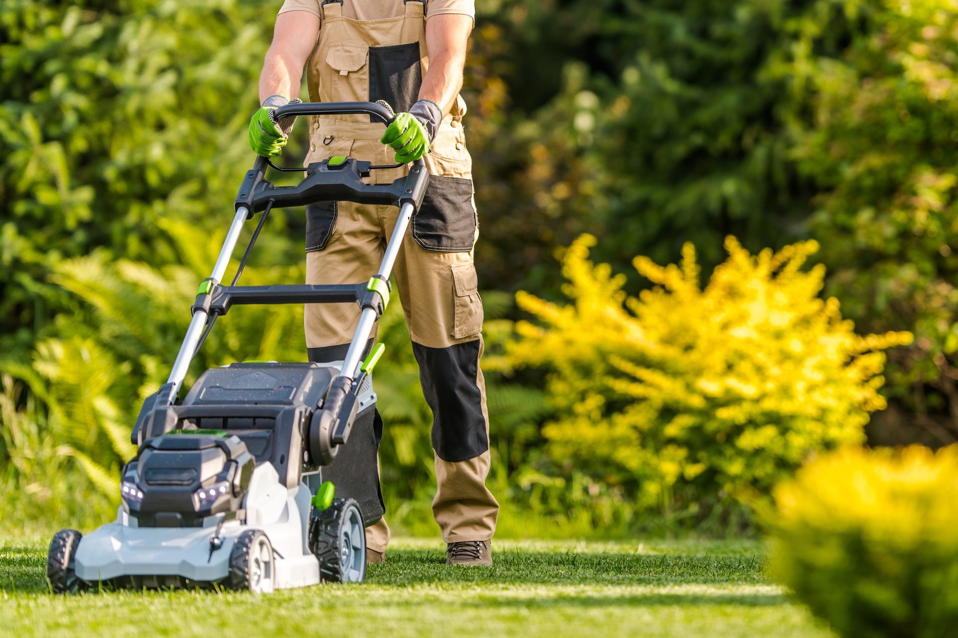 Person mowing a green lawn with a push mower in a sunny garden