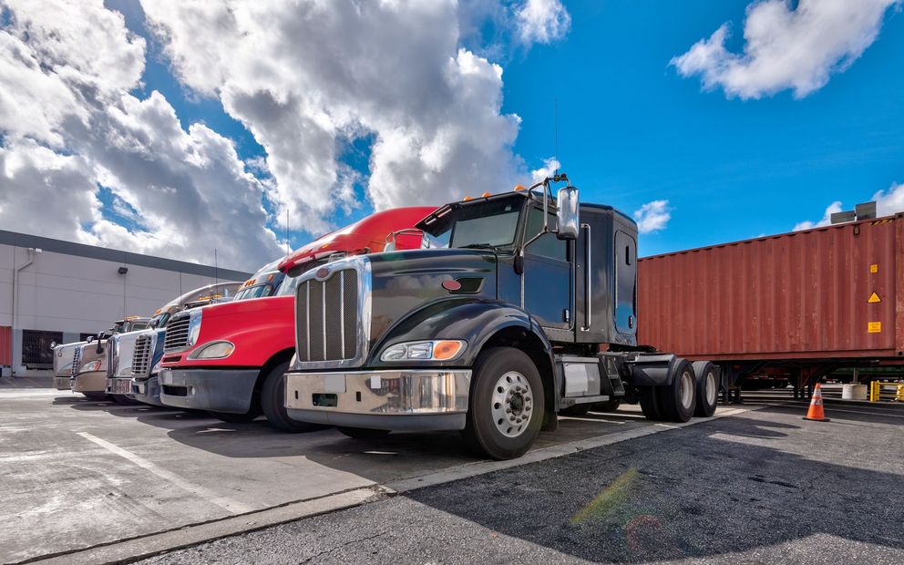 A row of semi trucks parked in front of a warehouse.