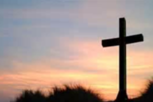 Silhouette of a cross at sunset against a pastel sky and dark horizon