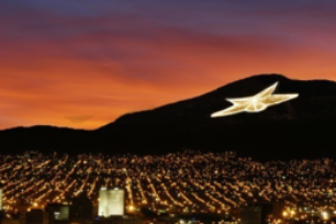 Sunset over a city with glowing lights and a large star-shaped light on a hillside
