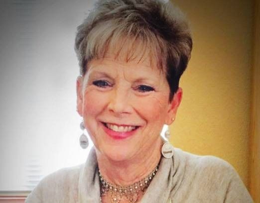 Smiling woman with short hair and earrings, seated indoors against a warm background
