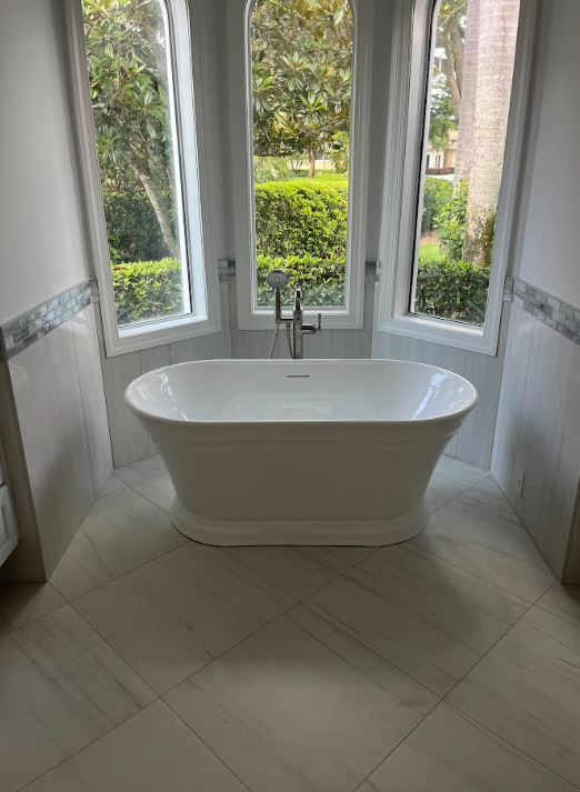 White freestanding bathtub in a bright bay-window alcove with garden view