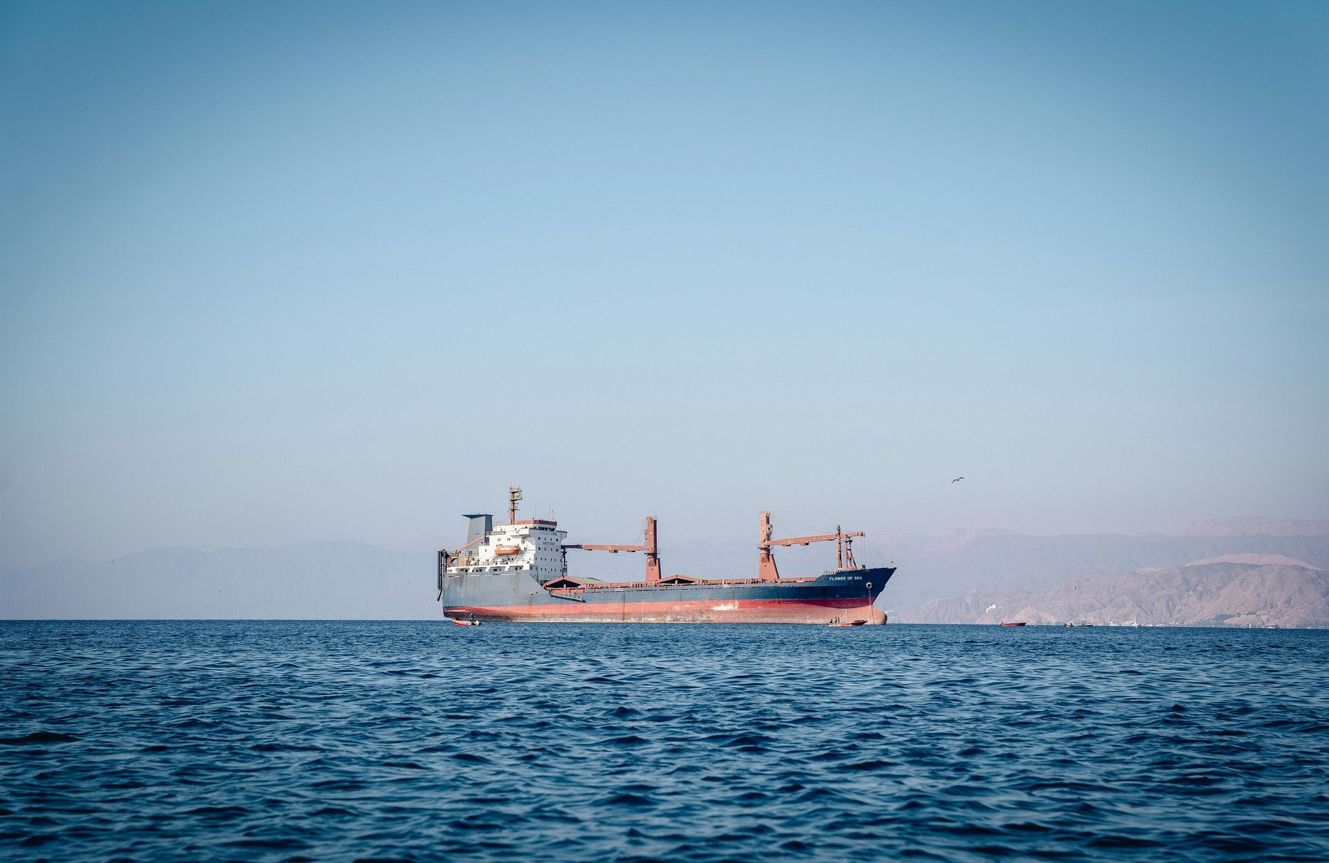 Frachtschiff auf ruhiger, blauer See mit ferner, dunstiger Küstenlinie unter klarem Himmel