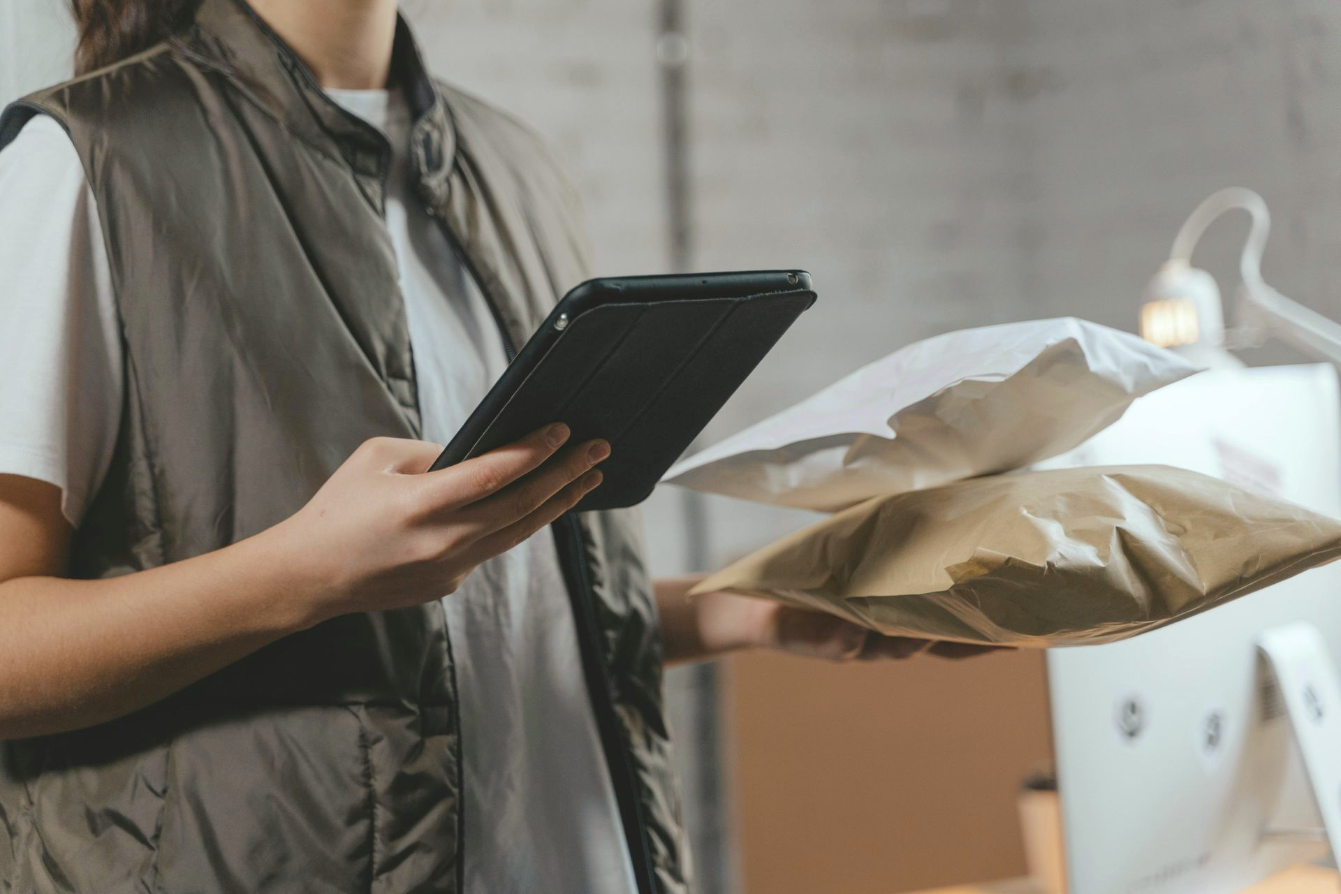 Eine Person hält ein Tablet in der Hand, während sie in einem Versandbereich Pakete packt.