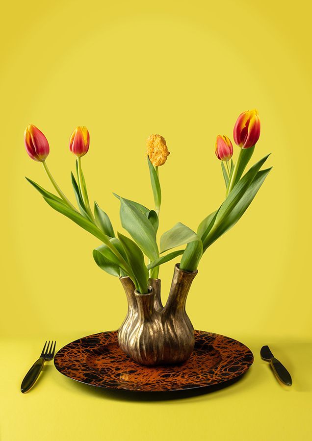 Tulpen in een gouden vaas op een gedecoreerd bord met een gele achtergrond en bijpassend bestek.