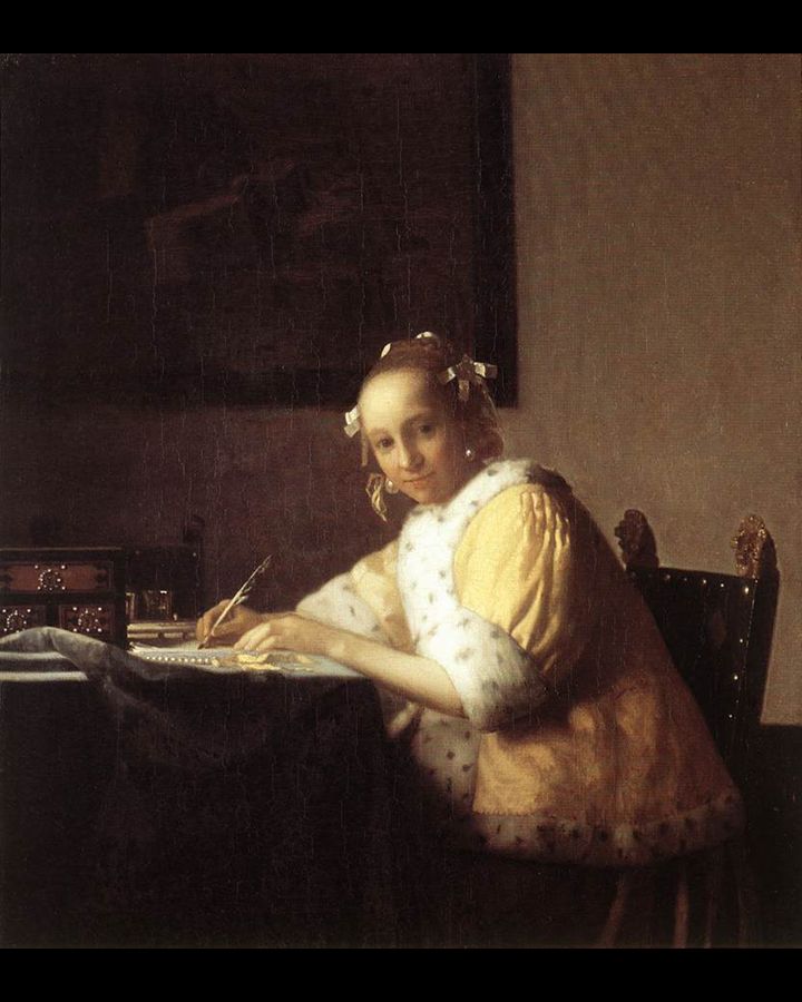 Vrouw schrijft aan een tafel, gekleed in een gele jas met witte bies. Interieur, donkere achtergrond.
