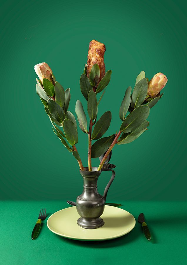 Kip en bladeren in een vaas op een groen bord, met vorken, tegen een groene achtergrond.