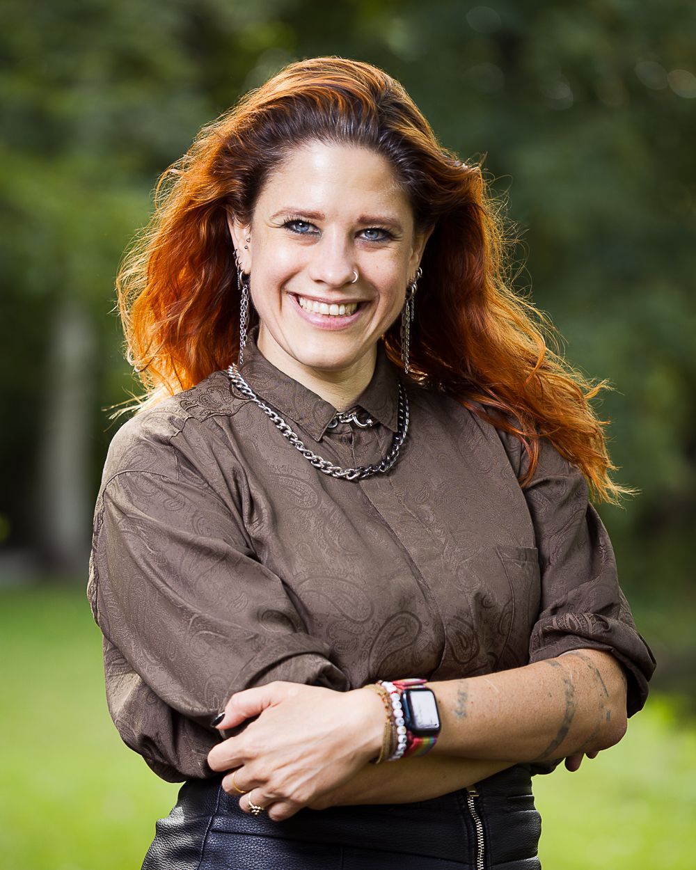Vrouw met rood haar en bruin shirt lacht buiten.