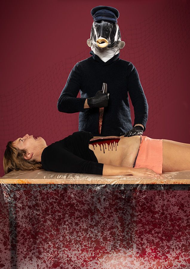 Een vis figuur en matrozenhoed houdt een bebloed mes boven een persoon die op een tafel ligt met een buikwond