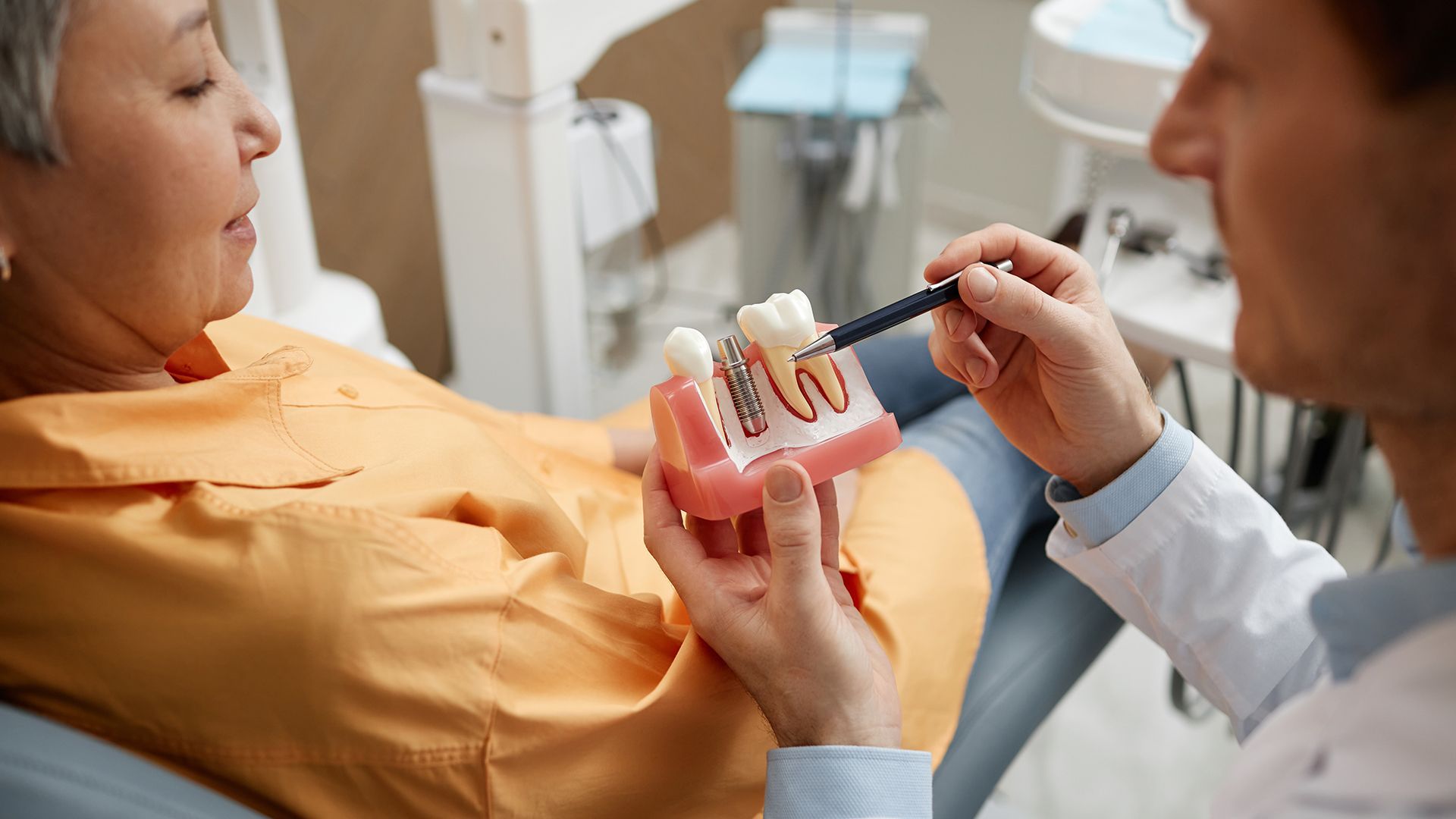 Dental model with two artificial teeth on metal screws, being held by tweezers.