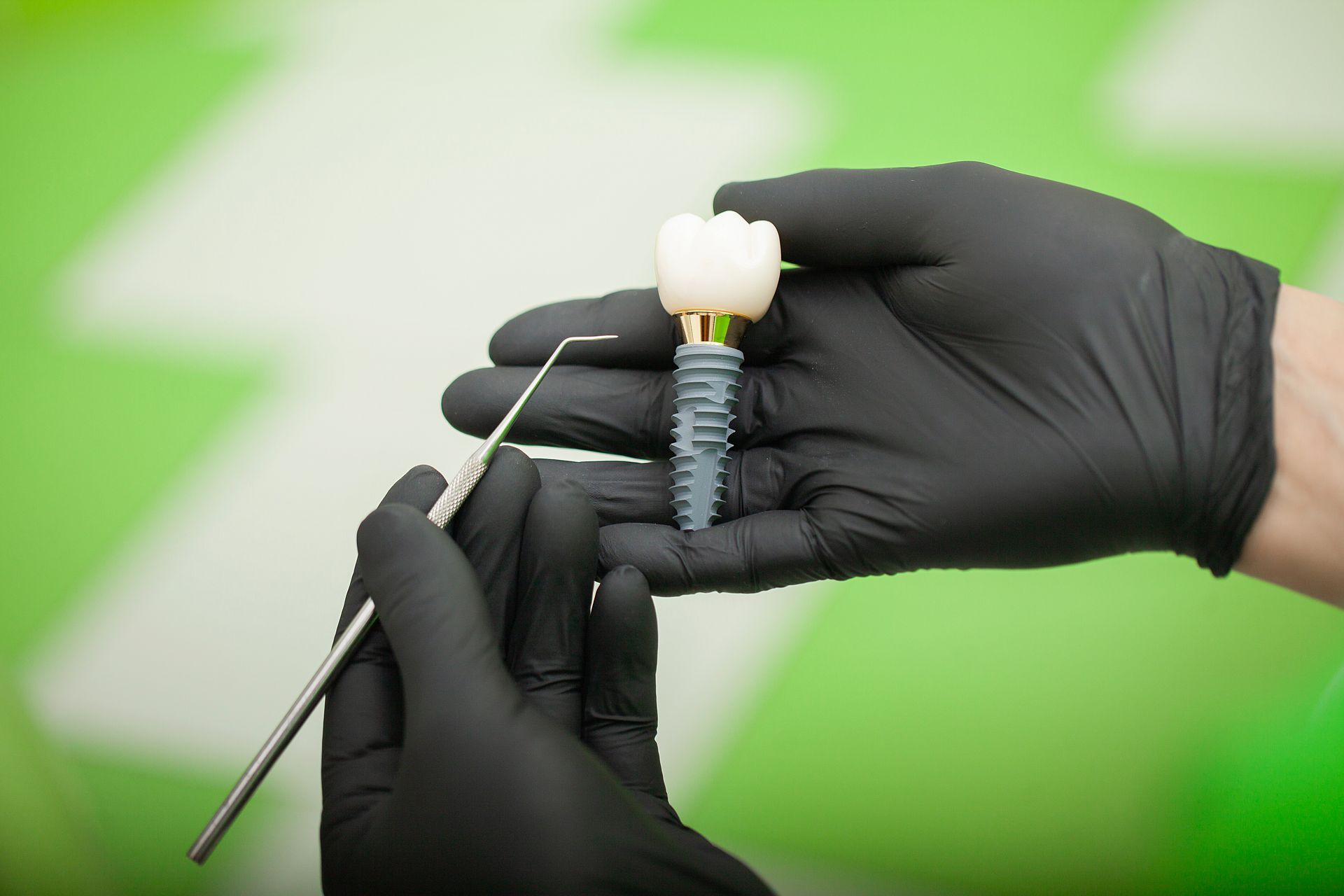 Gloved hands holding a dental implant with a screw and crown on a green background