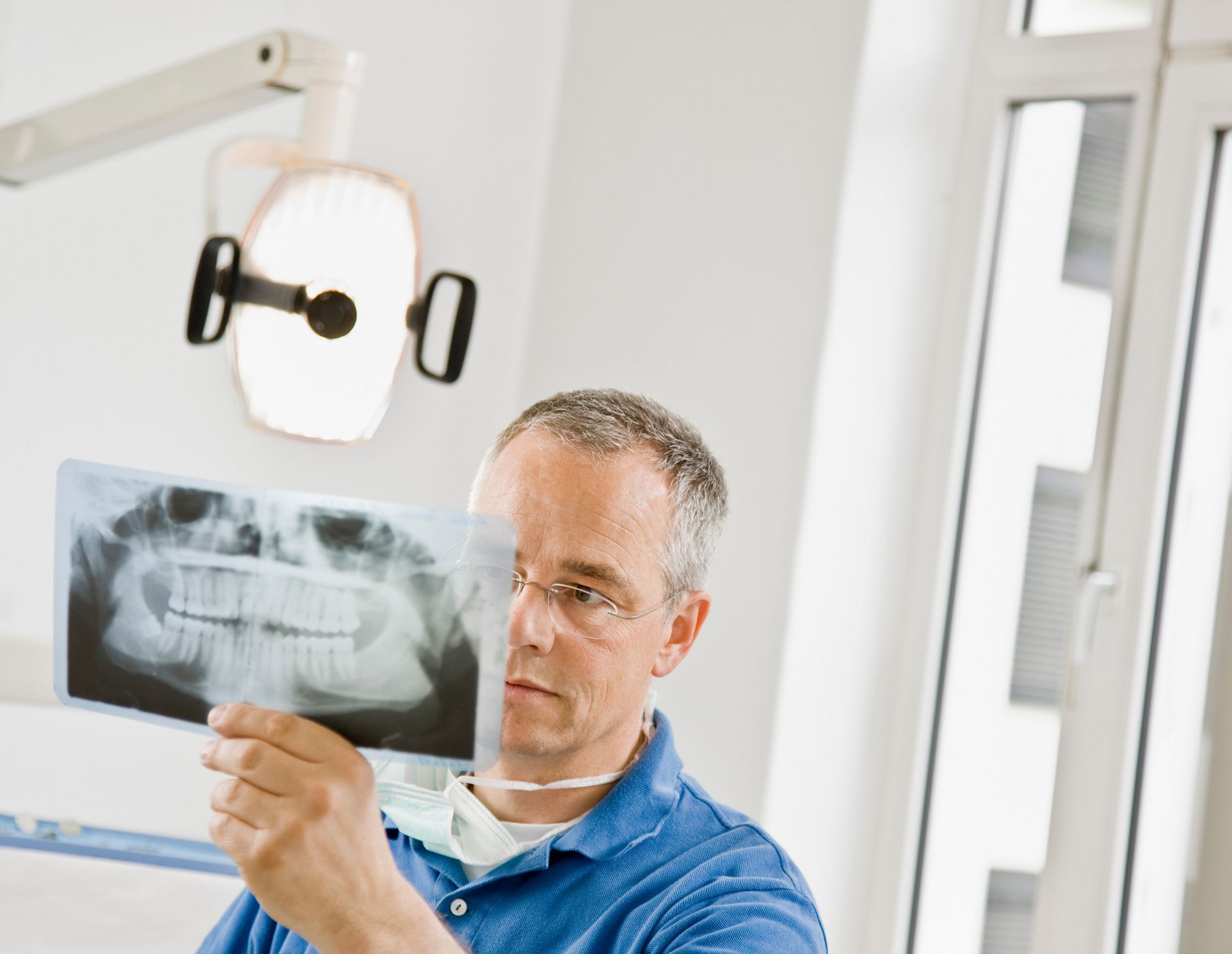 Dentist examining a panoramic X-ray under a bright clinic lamp