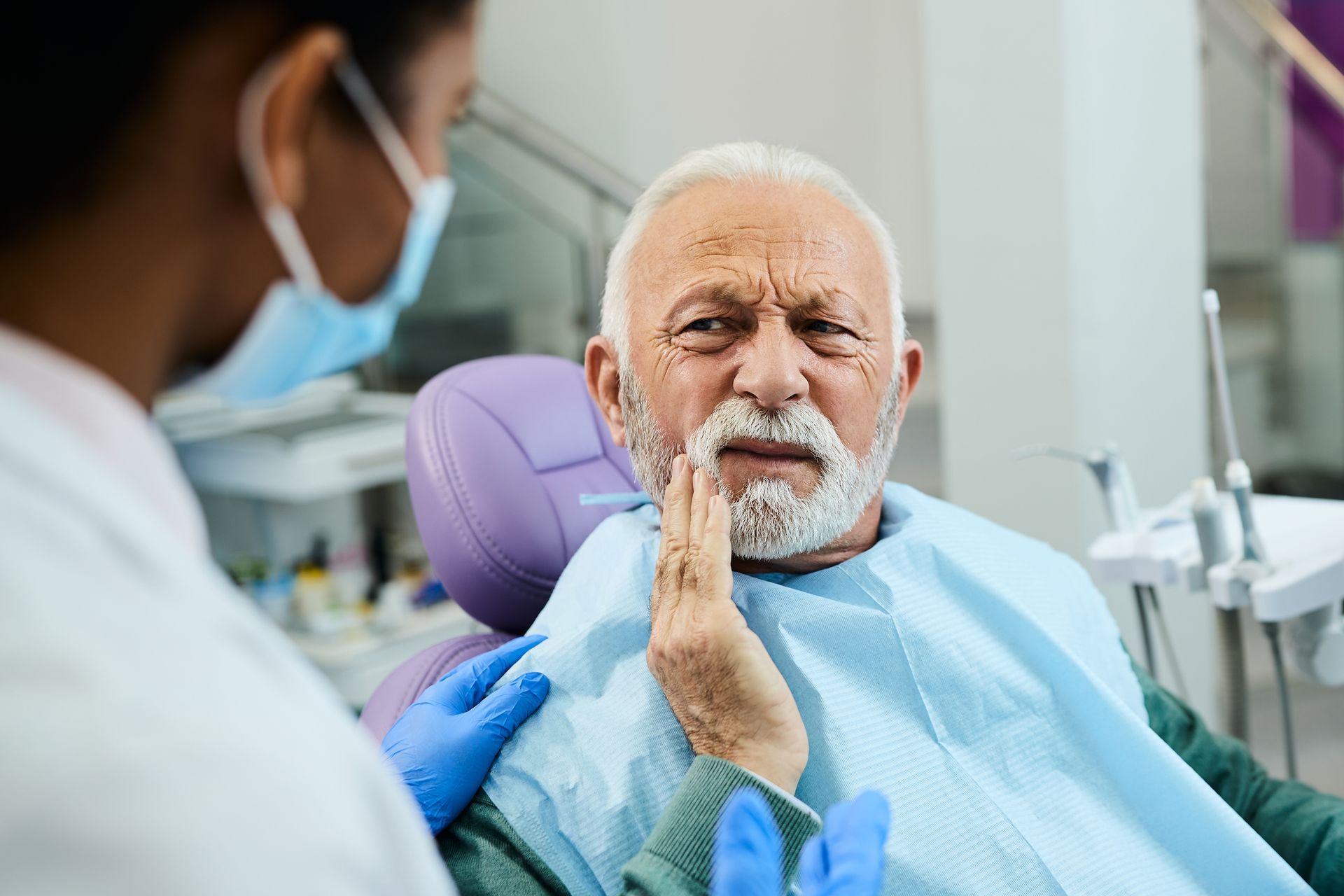 Dentist with blue gloves examines a patient seated in a dental chair