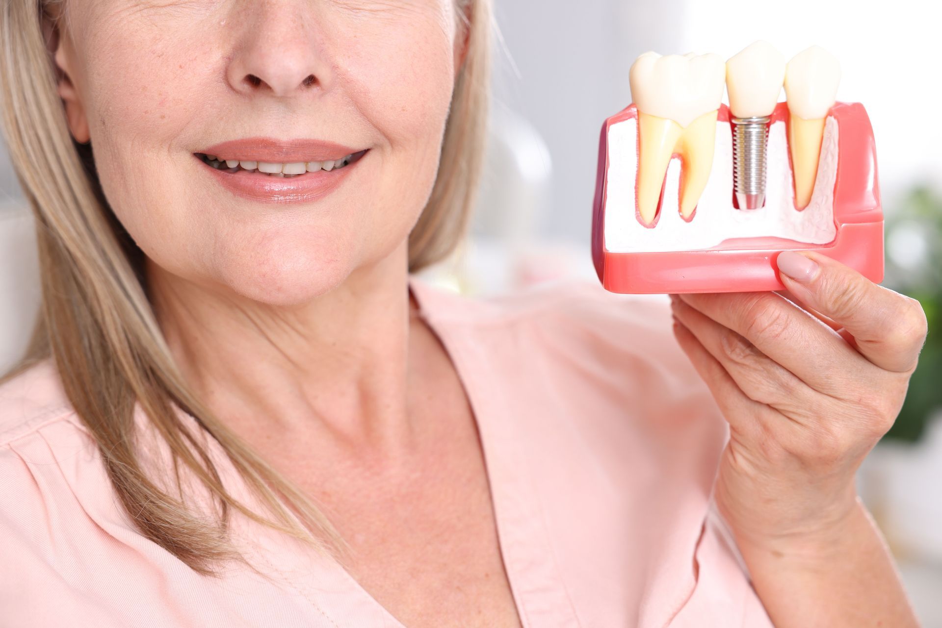 Woman holding a dental model showing teeth and gums, with a close-up of her smile and pink background