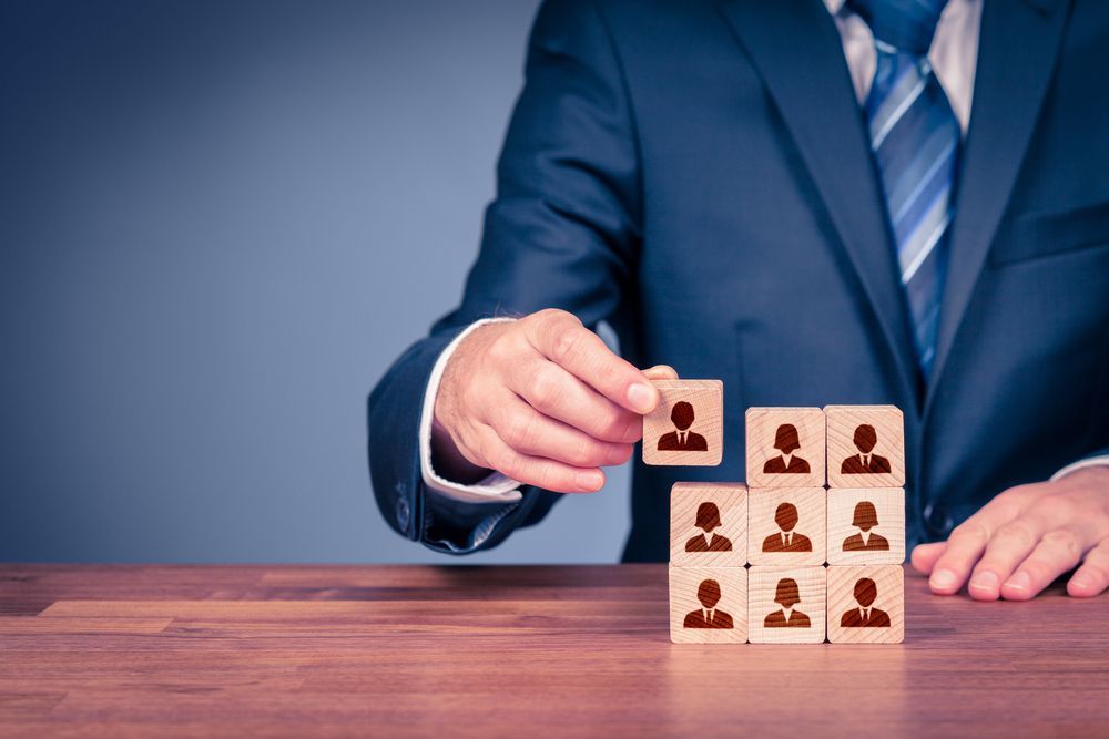 Person in Suit Arranging Blocks With Person Icons, Representing Team Building — People Assured Partners in Cannonvale, QLD