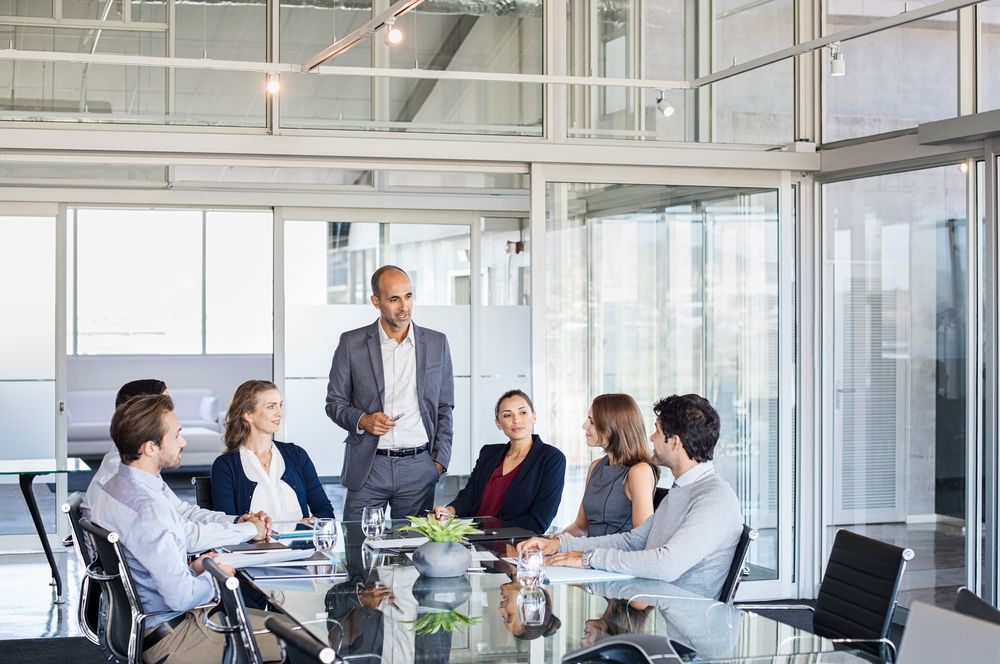 A Man in a Suit Leads a Meeting Around a Glass Table — People Assured Partners in Bowen, QLD