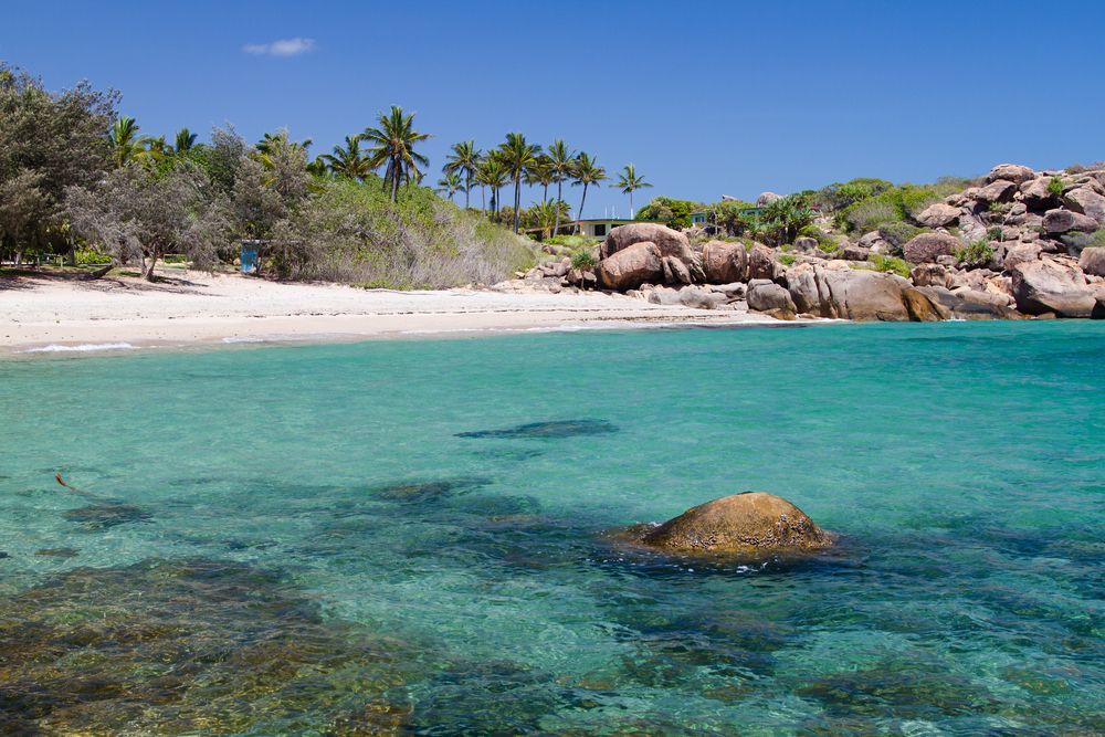 Turquoise Water at a Beach With White Sand, Trees, and Large Brown Rocks — People Assured Partners in Bowen, QLD