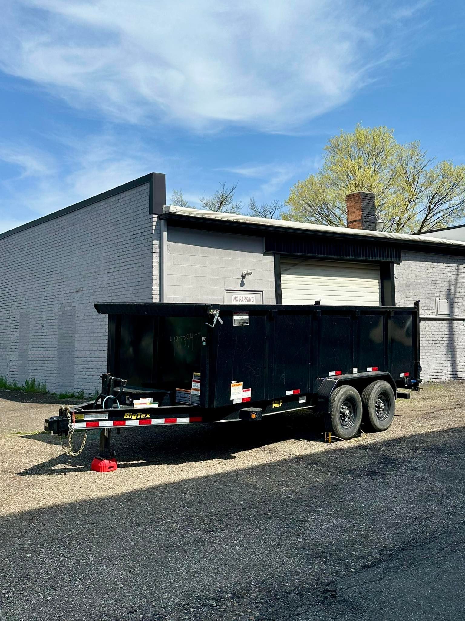 Black enclosed trailer parked on gravel beside a gray building under a blue sky.