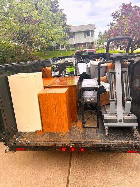Moving truck loaded with furniture and household items on a driveway, including chairs, boxes, and a stove.