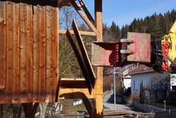 Rusty construction machinery beside a wooden building frame outdoors with a snowy mountain backdrop