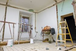 Renovation room with exposed walls, ladder, cement mixer, buckets, and unfinished floor