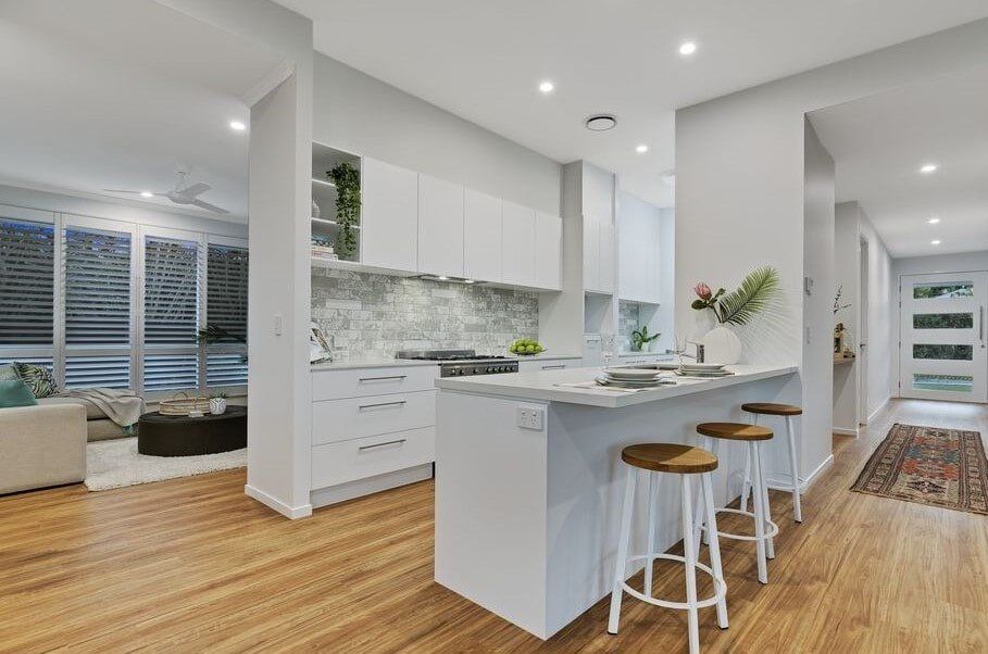 A Kitchen With White Cabinets And Wooden Floors And Stools — Norm Evans Floors Pty Ltd in Kunda Park, QLD