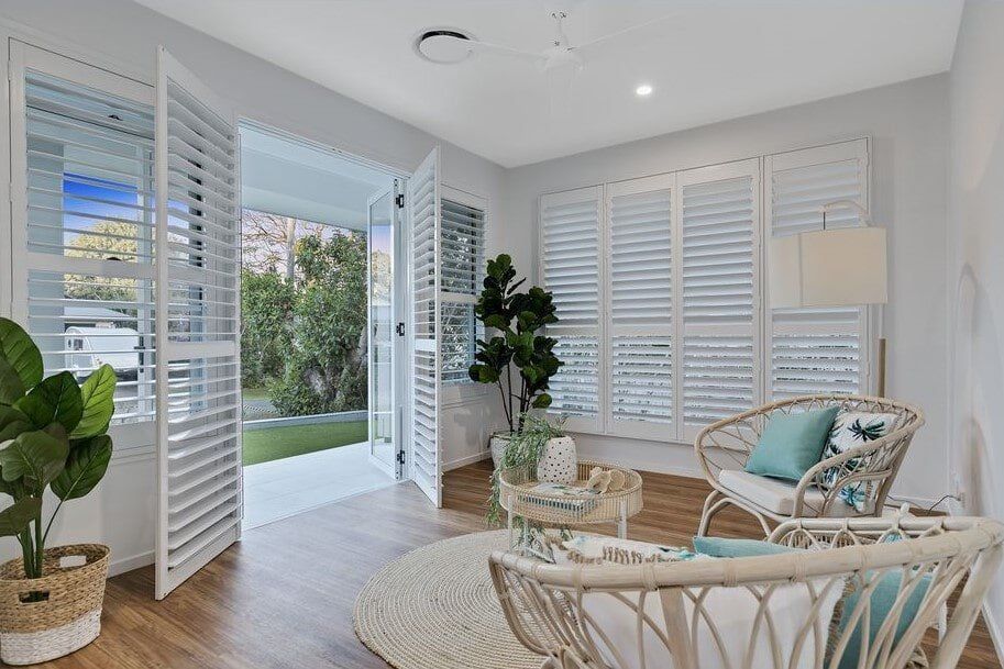 A Living Room With A Wicker Chair , Table And Shutters — Norm Evans Floors Pty Ltd in Kunda Park, QLD