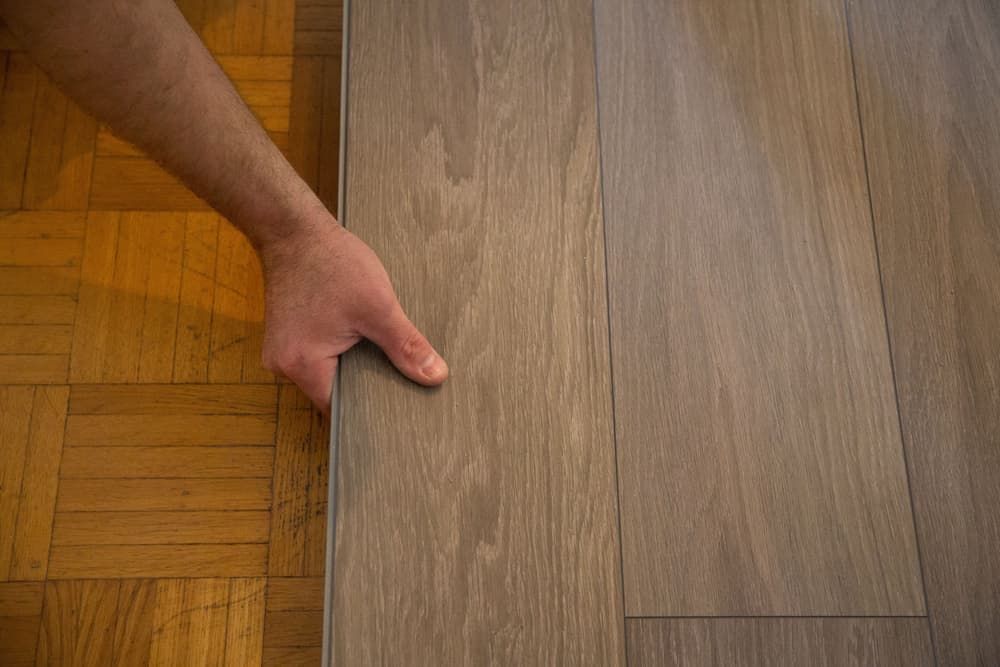 A Person Is Holding A Piece Of Wood On A Wooden Floor — Norm Evans Floors Pty Ltd in Caloundra, QLD