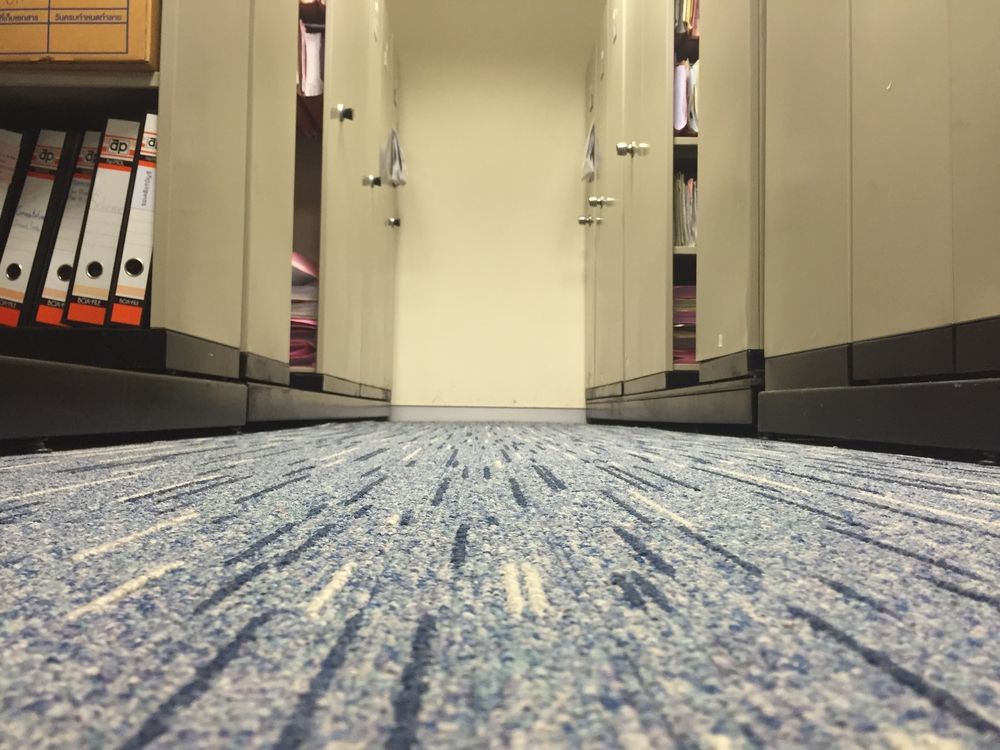Low-angle view of a narrow office aisle, lined with file cabinets on either side, blue carpet.
