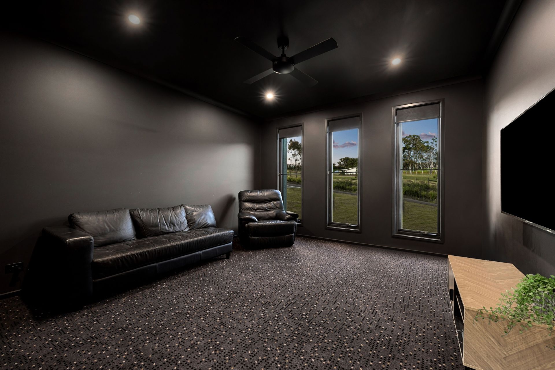 Modern living room with black sofa, recliner, ceiling fan, large windows, and wall-mounted TV — Norm Evans Floors Pty Ltd in Kunda Park, QLD
