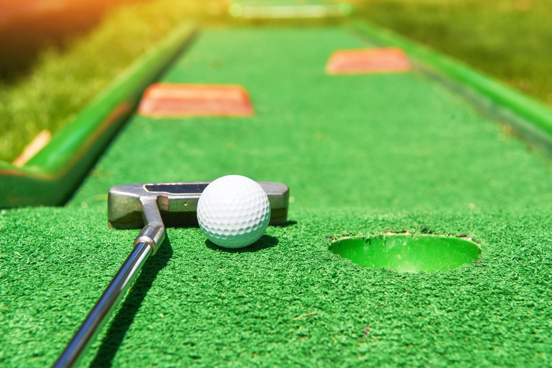Golf ball and putter on a green mini-golf course near the hole