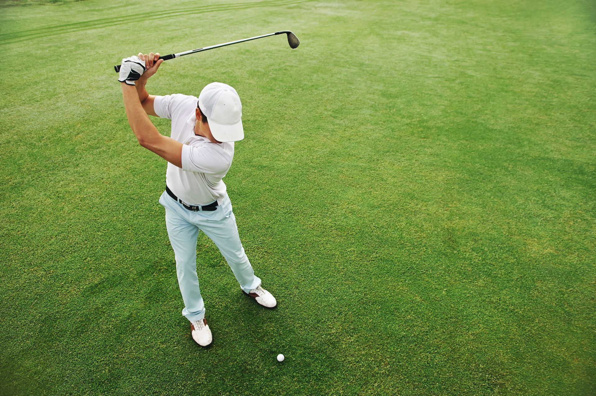 Golfer in white clothing swinging a club on a green fairway