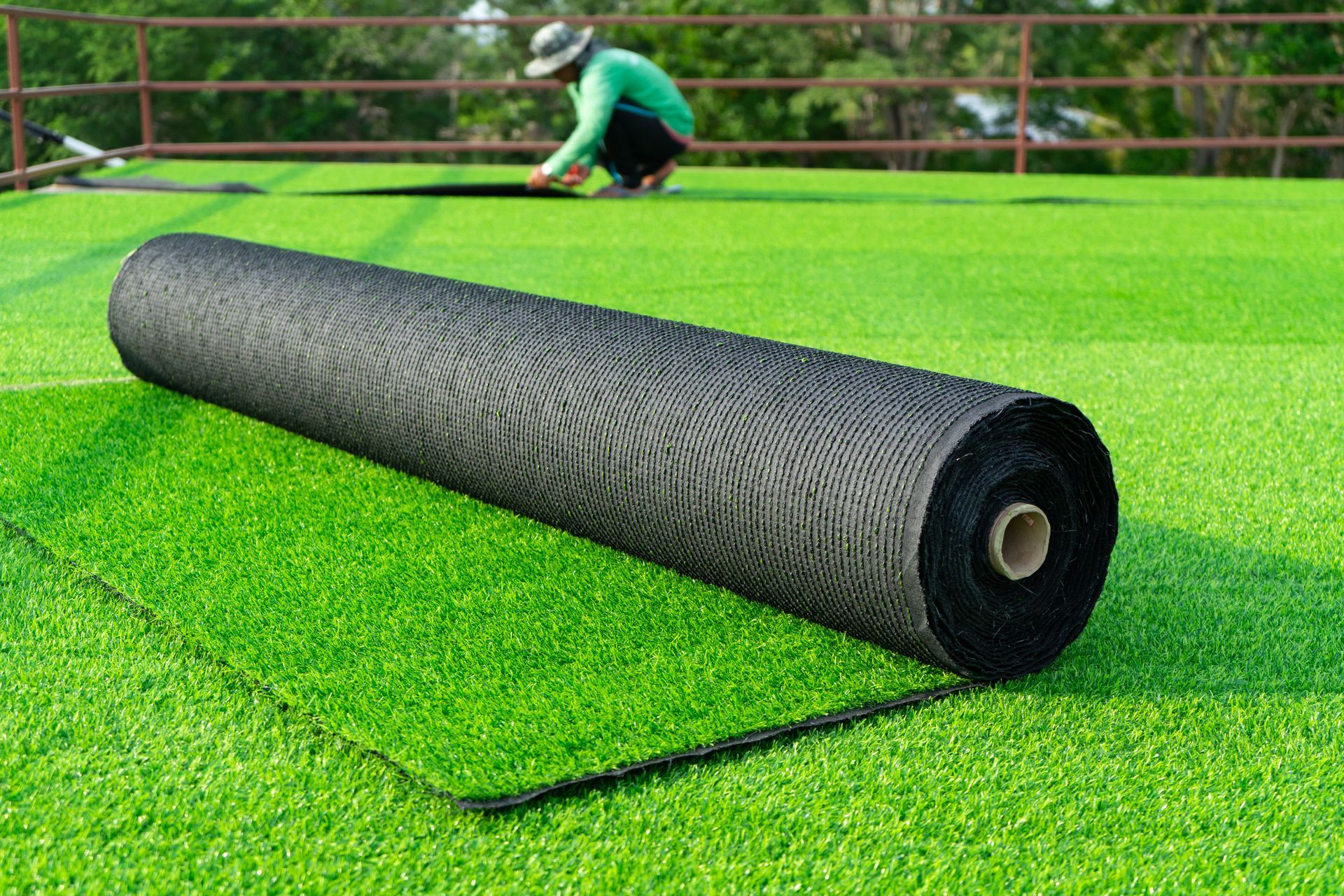 Person rolling out artificial turf on a bright green lawn