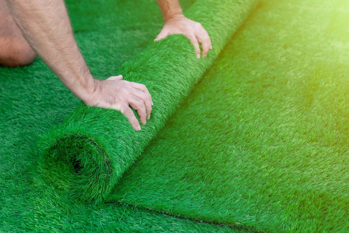 Hands rolling out green artificial turf on a lawn