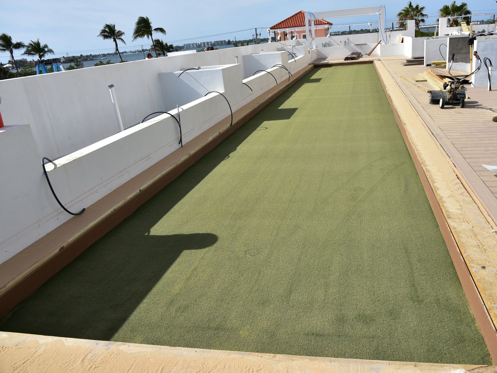 Green artificial-turf lane beside a white seaside wall with palm trees in the distance