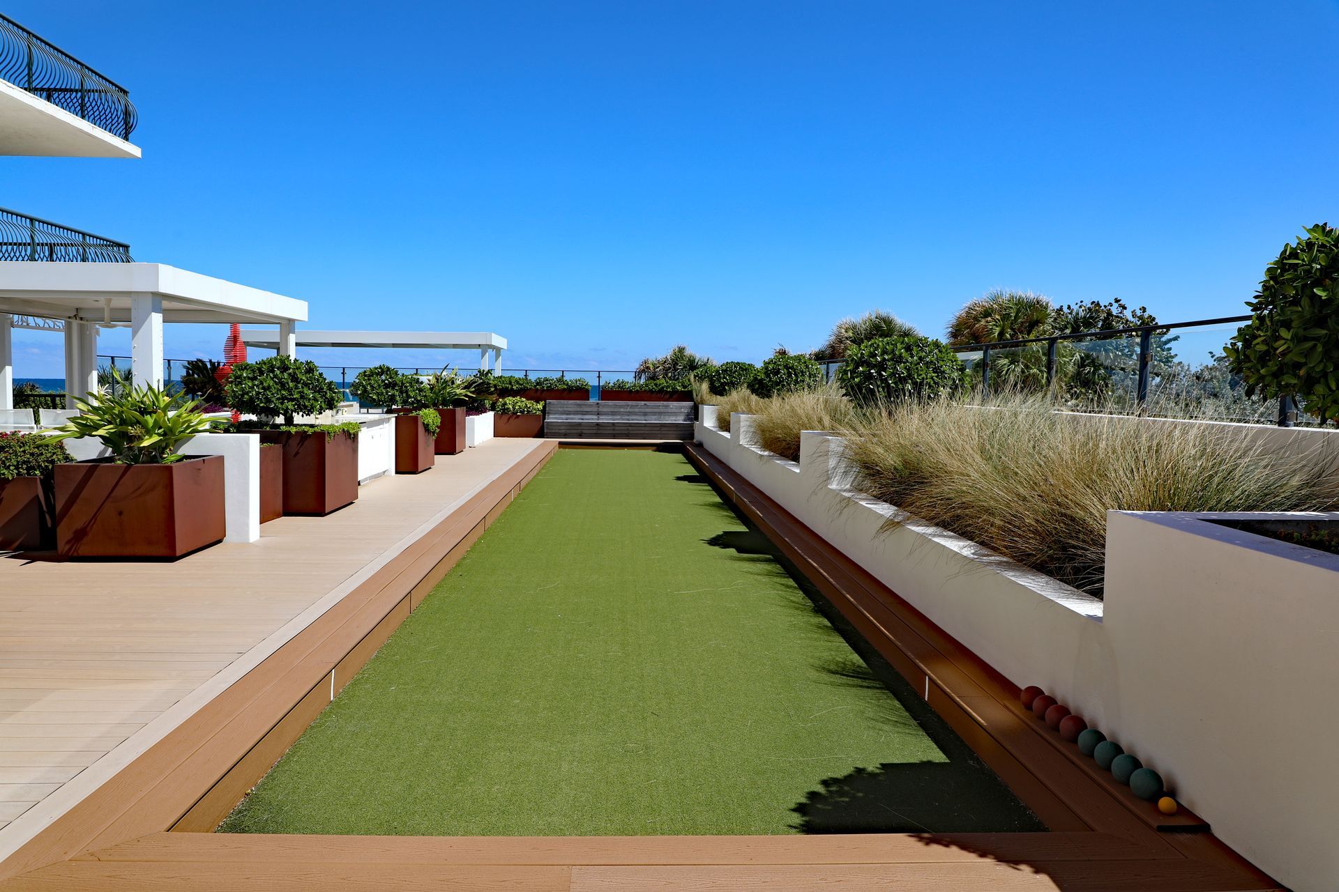 Modern rooftop terrace with artificial grass, planter boxes, and ocean view under clear blue sky