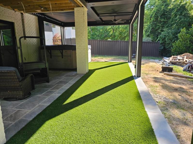 Workers laying green sod beside a house, with black soil and a lawn roller nearby