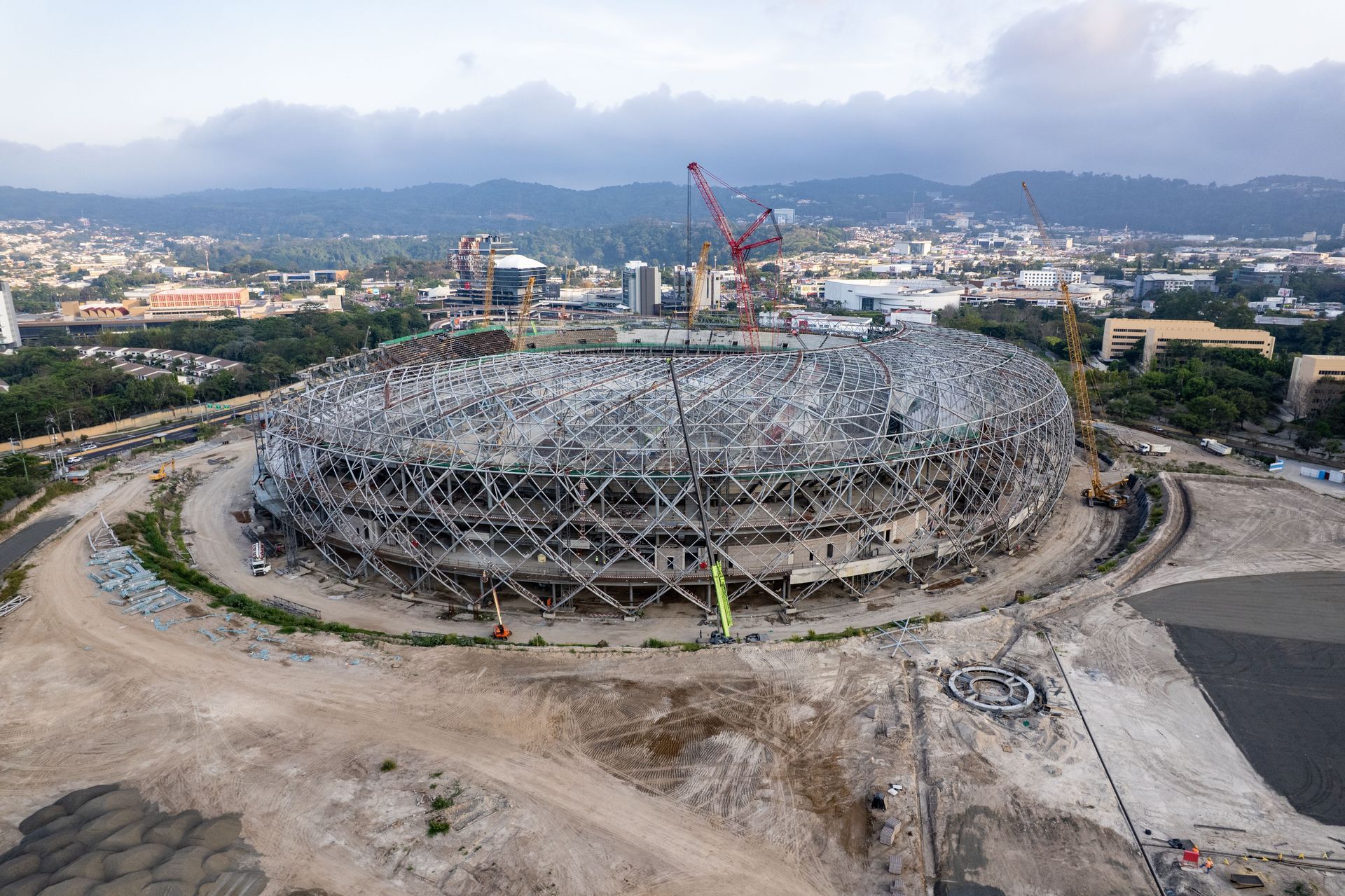 Aerial view of a large circular construction site with cranes and surrounding mountains in the distance