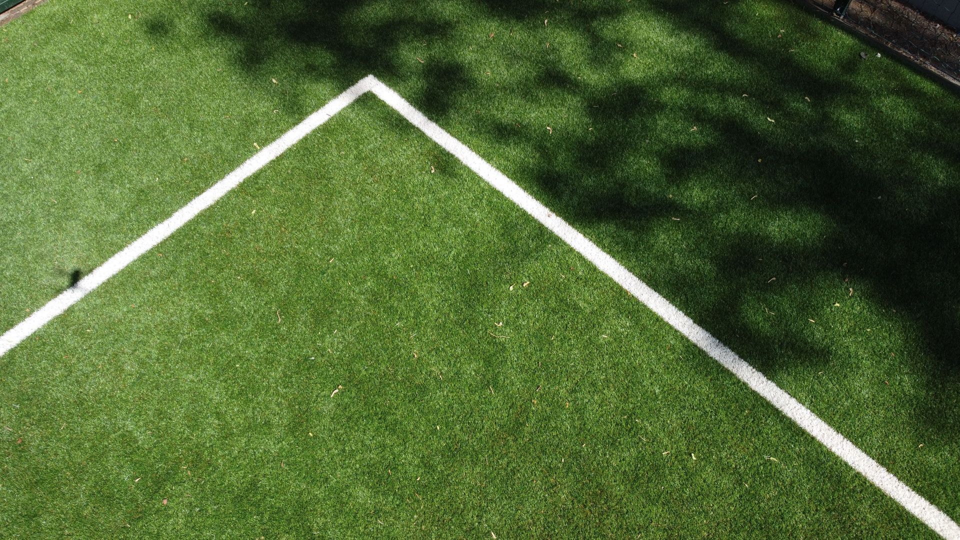White field corner lines on green grass, with shadows across the turf.