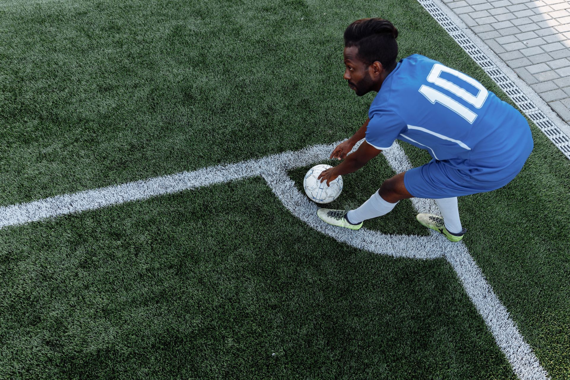 Soccer player in blue jersey placing the ball on the corner arc of a grassy field