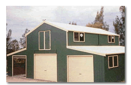 A two-story, dark green barn-style building with white trim, a gabled roof, two garage doors, and several windows.
