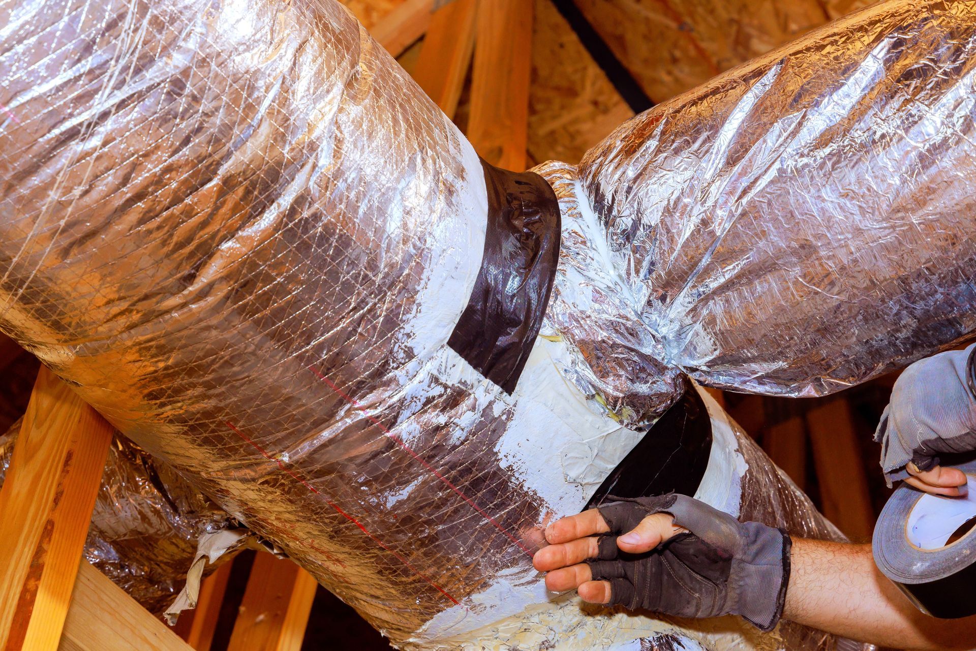 Person inspecting HVAC ductwork in an attic, wearing a glove and using their hand.