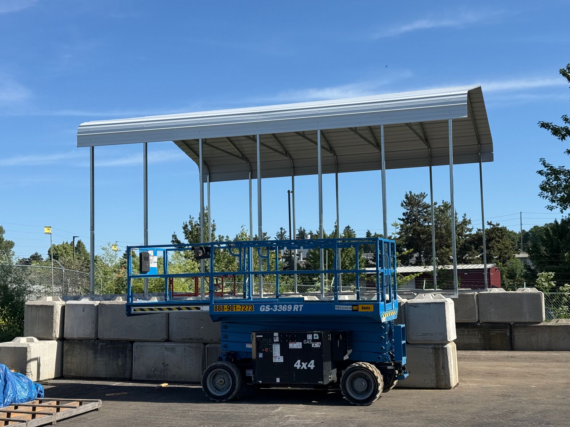 Blue lift platform parked beside stacked concrete blocks under a white canopy on a sunny day